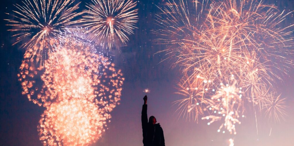 man holding up a sparkler with fireworks in the background